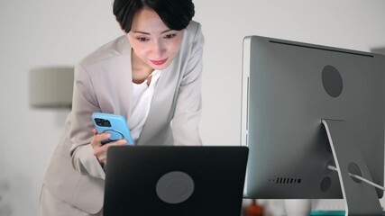 Poster - 暗いオフィスでスマホとパソコンを使って作業する女性ビジネスパーソン