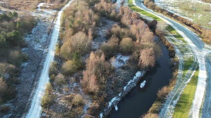 Wall Mural - Aerial view of a winding river surrounded by frost-covered pathways and trees in a serene winter landscape. The mix of snow, grass, and water creates a stunning natural contrast.