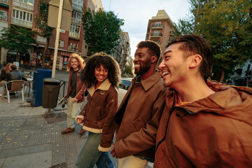 happy multiracial friends walking and laughing together in the city