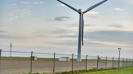Aufkleber - Clean energy generation with wind turbine rotating near electrical cabinet, standing behind protective fence under overcast sky, showcasing renewable power infrastructure in rural landscape
