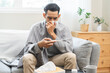 © KMPZZZ - Sick, influenza asian young man have fever blowing nose, sneezing in tissue, holding thermometer for check measure body temperature, ill while rest at home. Health care with disease, pandemic virus