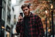 © Olena - Stylish Young Man with Beard in Black Flannel Shirt Engaged in Video Call on Urban Street