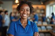 © Vadym - Happy African American retail clerk poses in commerce smiling at camera. Successful businesswoman stands indoor. Small business owner in blue uniform, sales success. Selling to clients supermarket