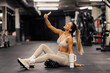 © Dusan Petkovic - Smiling fit female athlete sitting on a gym floor and taking selfies.