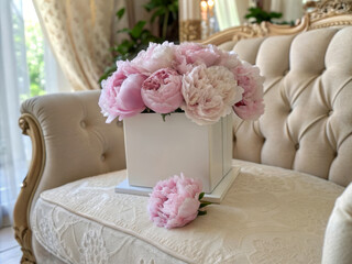 Poster - A beautiful arrangement of pink peonies in a white square vase resting on a stylish couch.