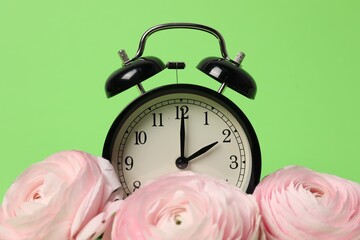 Poster - Spring time. Alarm clock and beautiful ranunculus flowers on green background, closeup