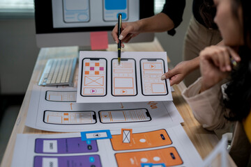 A woman is holding a pen and pointing at a paper with a phone design on it