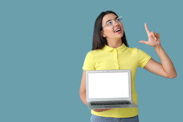 Wall Mural - happy young female programmer with laptop pointing at something on blue background