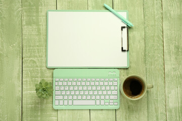 Wall Mural - clipboard, pen, tablet external keyboard and cup of coffee on green wooden background