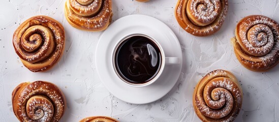 Poster - Top down view of golden brown cinnamon buns arranged around a white coffee cup on a light textured background with ample copy space for text
