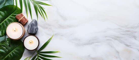 Poster - Relaxing spa setup with two candles on a marbled surface, surrounded by green palm leaves and smooth stones in soft natural light.