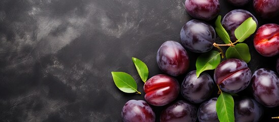 Poster - Ripe dark purple plums with green leaves arranged on a black textured surface, showcasing a fresh and vibrant fruit composition.
