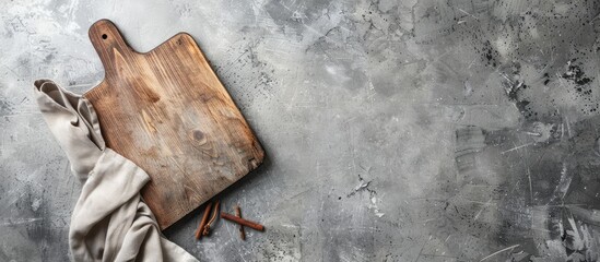 Poster - Top down view of a rustic wooden cutting board on a textured grey concrete surface with a light grey napkin on the left creating ample copy space.