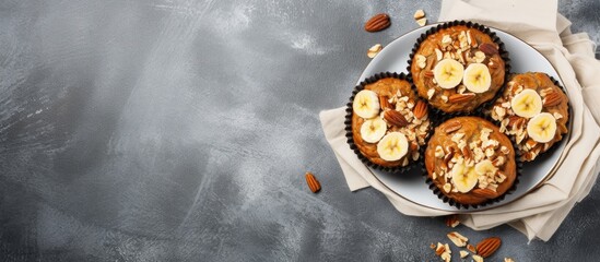 Poster - Healthy banana muffins with oatmeal and walnuts in black liners on a light gray plate with sliced bananas, set on a dark gray concrete background.