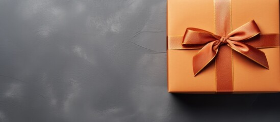 Poster - Orange gift box with a brown ribbon positioned in the upper left corner on a dark concrete background featuring ample copy space to the right.