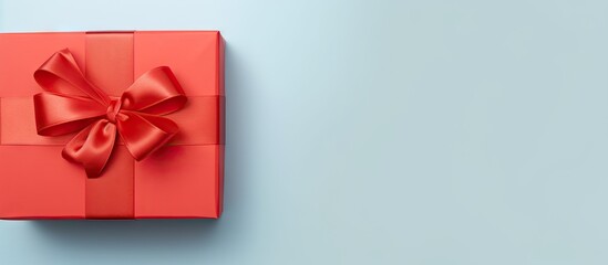 Poster - Gift box with a glossy red ribbon bow positioned top left on a soft blue background ideal for celebrations with ample copy space on the right