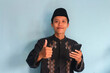 © Lailar Studio - Happy smiling Asian Muslim man holding cell phone with thumbs up gesture