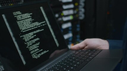 Cropped shot of unrecognizable IT specialist holding laptop with running program code on screen checking work of mainframe computer in data center