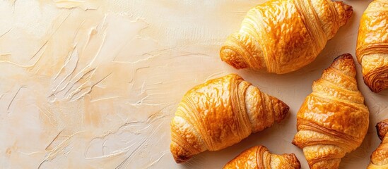 Poster - Golden baked croissants arranged on a textured beige background with soft highlights showcasing their flaky layers and appetizing shine.