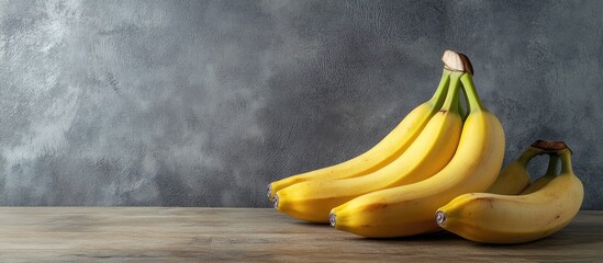 Poster - Fresh yellow bananas arranged on a rustic wooden table against a textured gray wall background, showcasing their natural beauty and ripeness.
