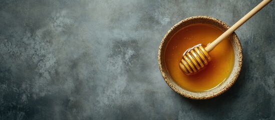 Aufkleber - Aerial view of a shallow bowl filled with golden organic honey and a wooden dipper on a textured dark stone surface with soft lighting
