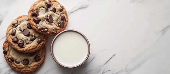 Poster - Delicious chocolate chip cookies with melted chocolate chunks beside a round bowl of milk on a light marble surface, top view layout