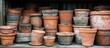 © meristock - A rustic display of weathered terracotta plant pots in various sizes stacked in a wooden shed with a green backdrop reflecting aged charm.