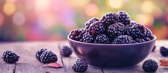 Poster - Bowl of fresh blackberries positioned centrally on a wooden table with a soft blurred colorful background featuring warm tones and bokeh effects.
