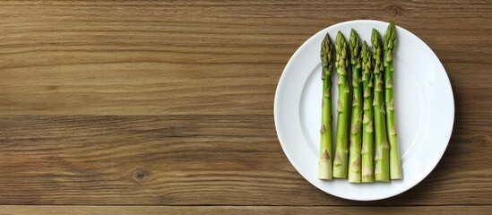 Poster - Fresh asparagus arranged on a white plate on a wooden surface, showcasing varying stages of maturity, with a clear area for text on the left.