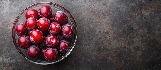 Poster - Fresh cherry plums in a clear glass bowl positioned centrally on a dark textured table surface with ample copyspace on the right side