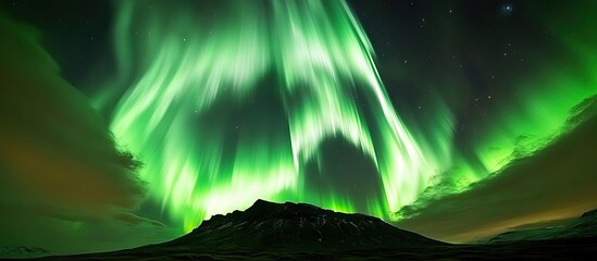 Wall Mural - Vibrant green Northern Lights dance over a dark rugged mountain under a starry sky, creating a mesmerizing celestial display at night.