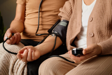  Two family members sit together on a couch while one takes the other's blood pressure. The atmosphere is warm and caring, focusing on health and well-being