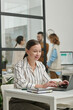 © Mediaphotos - Vertical portrait of smiling young businesswoman using computer at desk and enjoying work in office