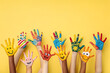 © GTNA73 - A Lot of painted hands raised up. Group of multiracial funny children funny kids hands up on the yellow background. Copy space.