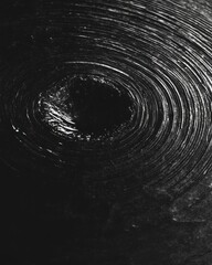 Fototapete - Abstract grayscale image featuring a swirling, concentric circular pattern leading to a dark center. The texture is slightly grainy, creating a sense of depth.