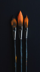 Poster - Three paintbrushes with orange paint lying on a black background, representing art, creativity, and painting