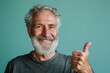 © Markus Schröder - Portrait of a happy man in his 60s showing a thumb up on soft teal background