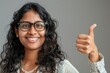 © Markus Schröder - Portrait of a jovial indian woman in her 40s showing a thumb up while standing against soft gray background