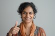 © Markus Schröder - Portrait of a jovial indian woman in her 40s showing a thumb up isolated in soft gray background