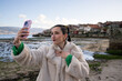 © asier - Young stylish woman capturing selfie near coastal town of combarro, enjoying sunny beach moment during travel adventure in galicia, spain