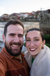© asier - Young couple capturing selfie moment with traditional stone houses of combarro, historic coastal village nestled in galicia, spain