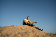 © asier - Female guitarist perching on rocky ledge, strumming acoustic instrument during golden hour sunset, warm light bathing punta faxilda landscape with peaceful ambiance