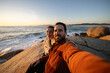 © asier - Loving couple capturing sunset selfie on rocky coastline, sharing intimate moment against dramatic punta faxilda seascape in galicia, spain