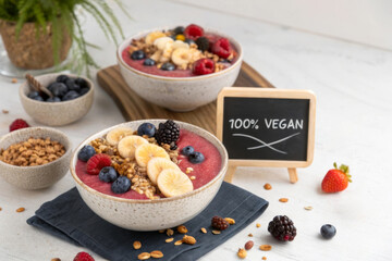 Poster - A vibrant display of vegan smoothie bowls topped with fresh fruits and granola, alongside a small chalkboard sign that reads '100% VEGAN.'