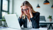 © Fox_Dsign - a woman holding her head because of a migraine, sitting at a desk in front of her computer