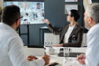 © pressmaster - Side view portrait of mature female medical professional pointing at virtual conference screen during online team meeting