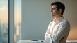 © Ocelia_Mg - A young professional stands thoughtfully by a large window in a modern office. The warm glow of sunset casts reflections, enhancing a moment of contemplation and planning for future projects