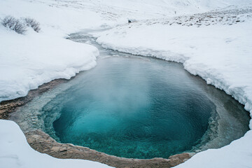 Wall Mural - Pristine geothermal hot spring surrounded by snow in a serene winter landscape, featuring a mesmerizing deep blue water hue and steaming surface.