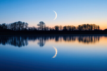 Wall Mural - A serene crescent moon rises over a silhouette of trees, reflecting on the calm waters of a tranquil lake at twilight.