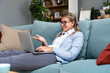 © Srdjan - Young beautiful business woman lying on couch using laptop computer in home office apartment, working online, having video call. Creative female smiling, checking social media, typing message.